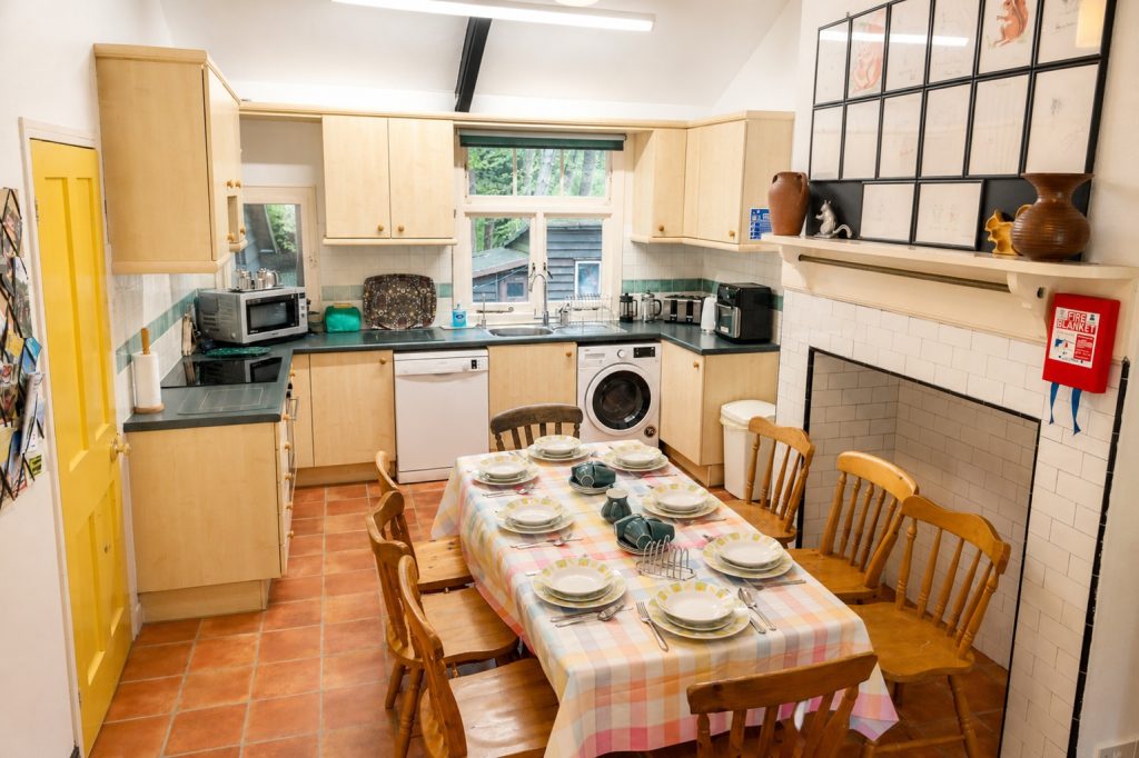 Large fully-equipped double-aspect kitchen, with dining table, overlooking lawn at front at woodland at back